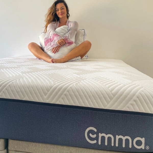 Moça sentada ao fundo da cama com travesseiro Antiestresse Emma.
