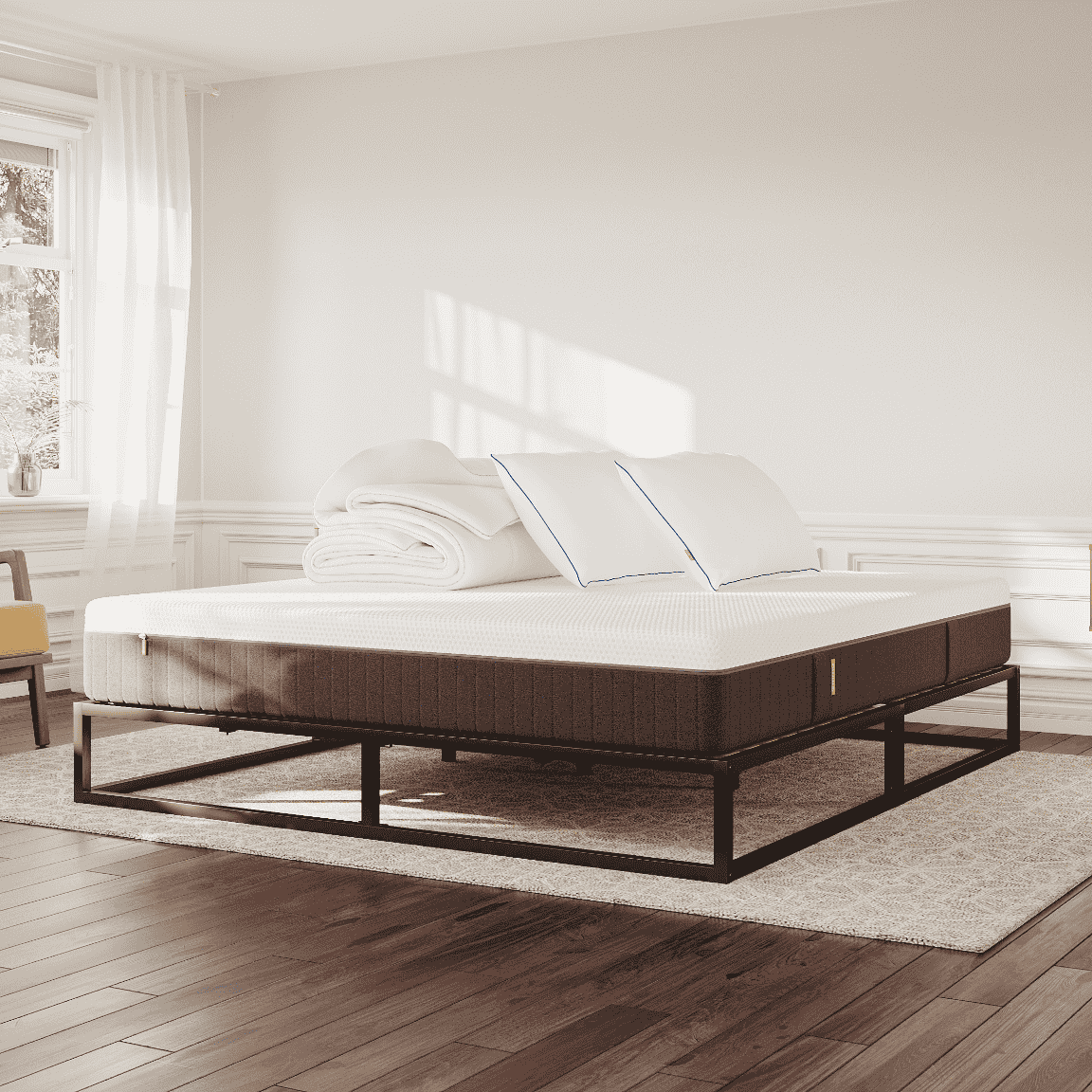 Licht en modern ingerichte slaapkamer met een Emma metalen bed, witte lakens, twee kussens en een opgevouwen dekbed; zachte natuurlijke lichtinval.