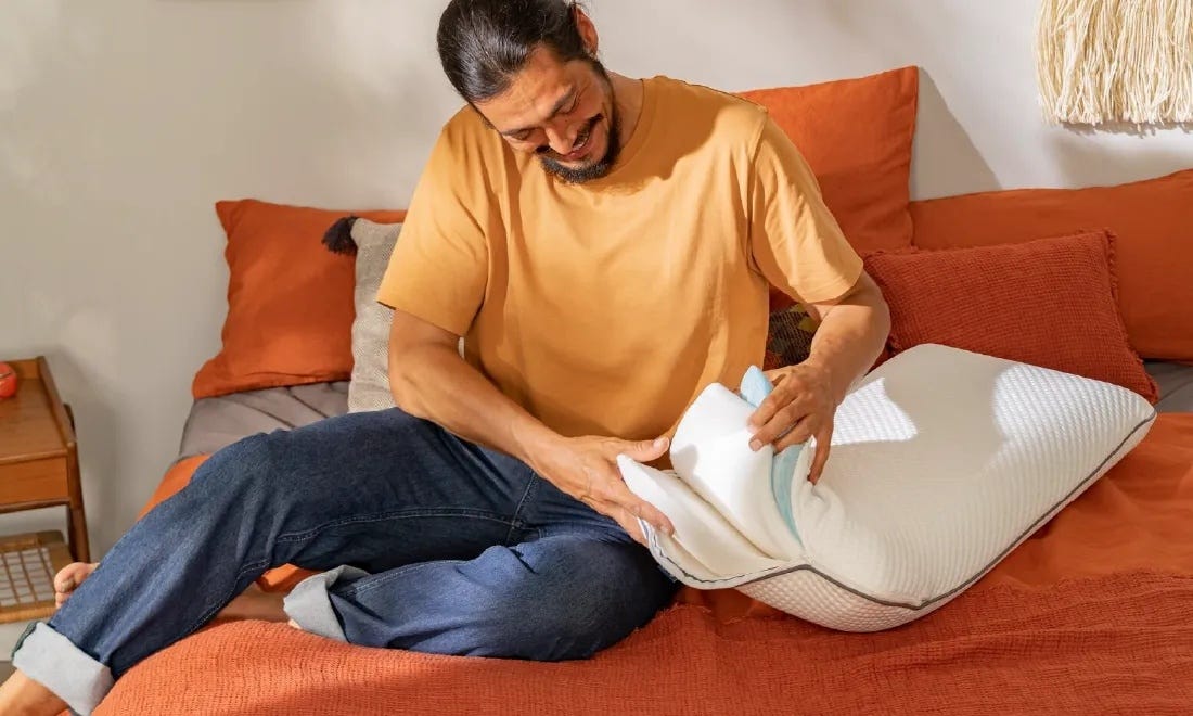 Persona seduta su letto arancione mentre osserva un cuscino bianco.