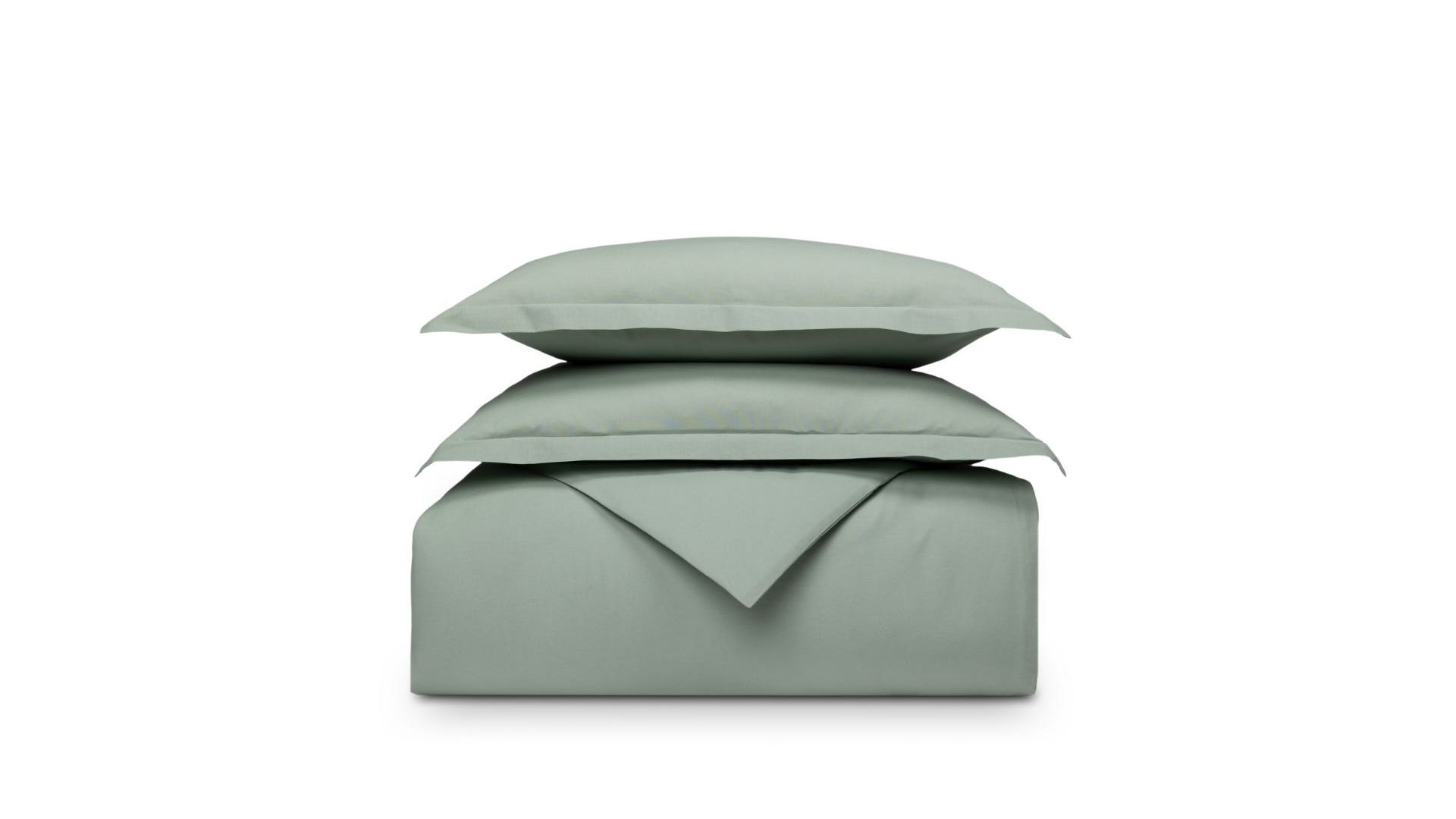 Set di biancheria piegato verde su sfondo bianco, cuscino sopra il piumone.