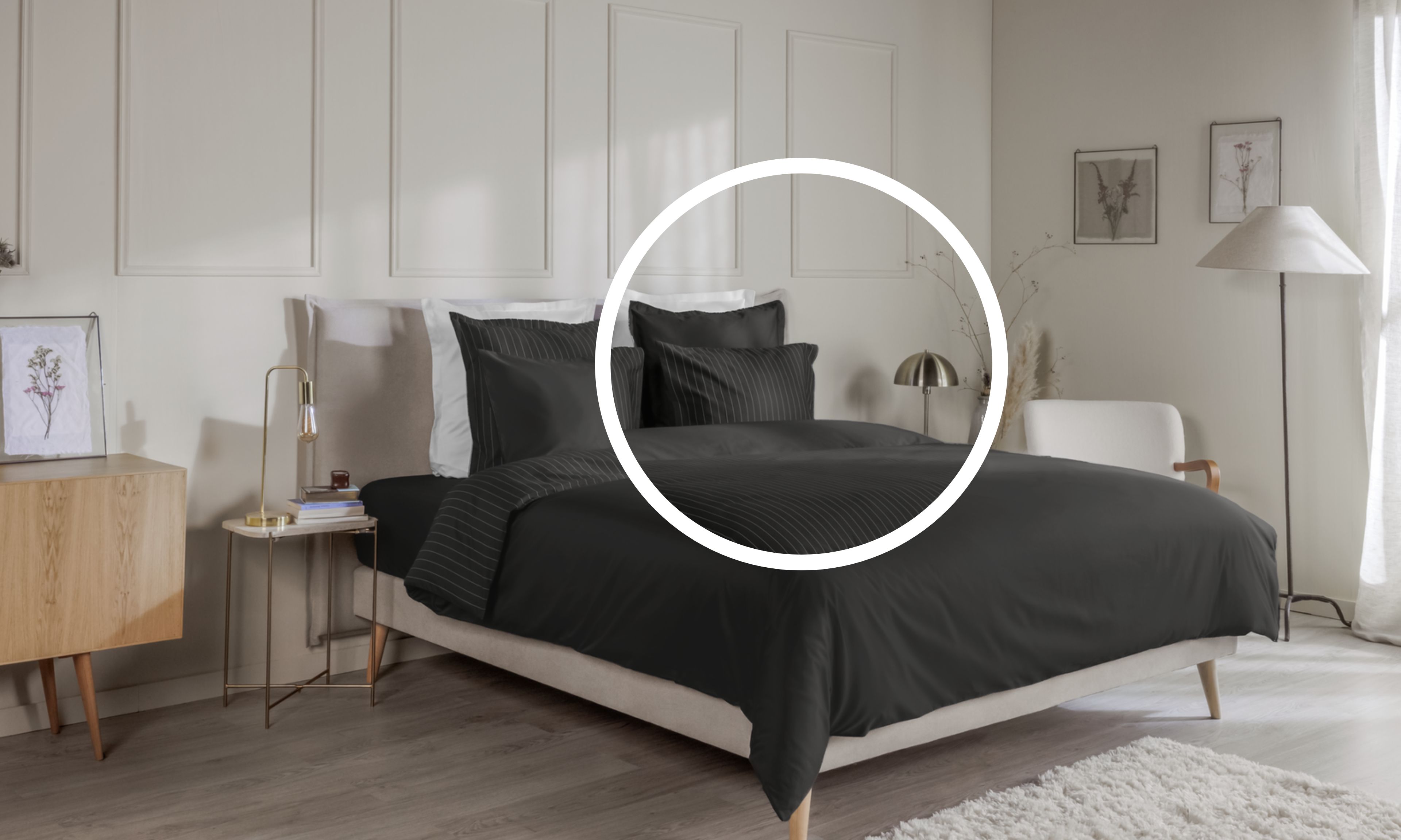 Letto ordinato con biancheria a righe bianche su grigio scuro, in una camera decorata con mobili e quadri.