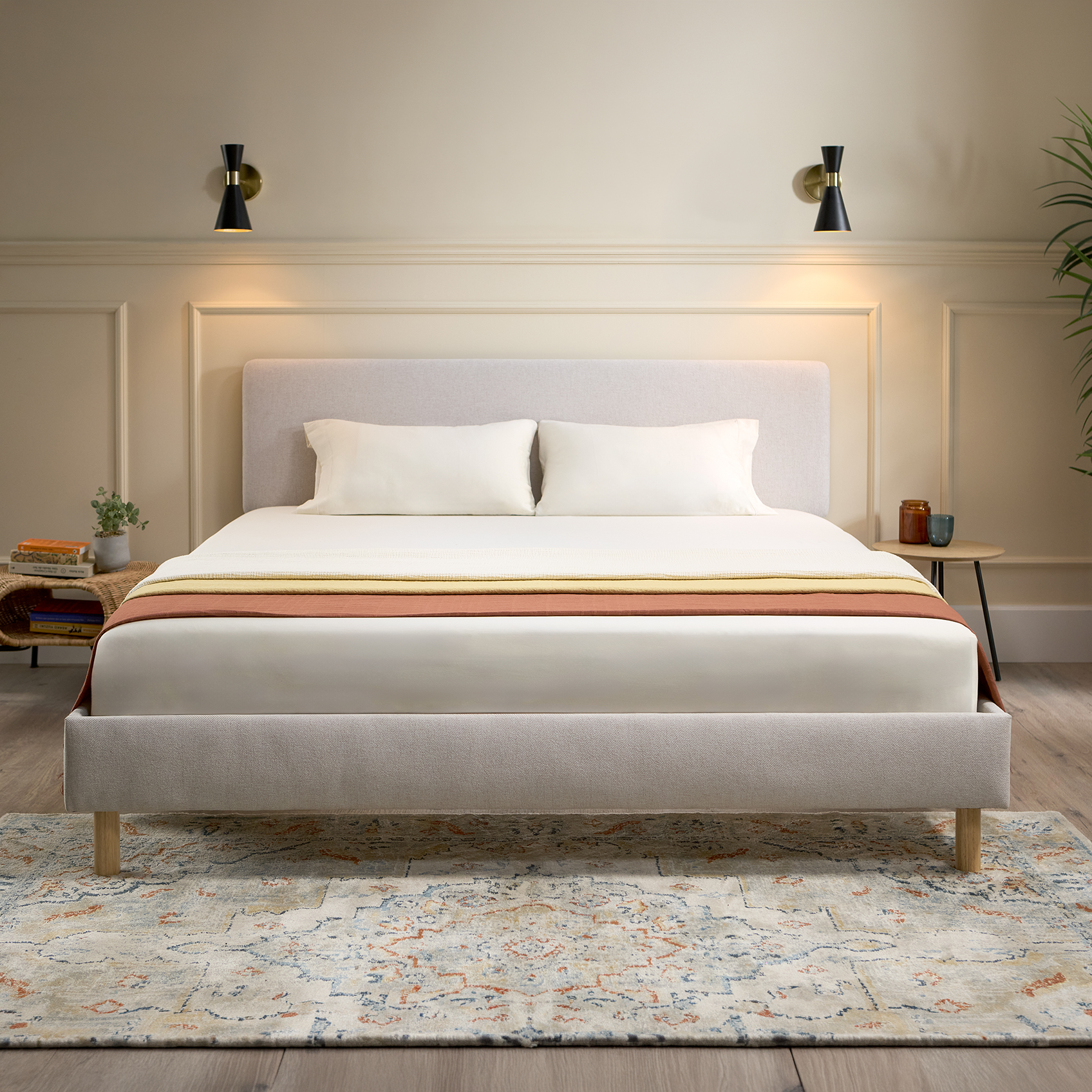 Emma Boxbed in beige with upholstered headboard and wooden legs, styled in a warm Scandinavian bedroom.