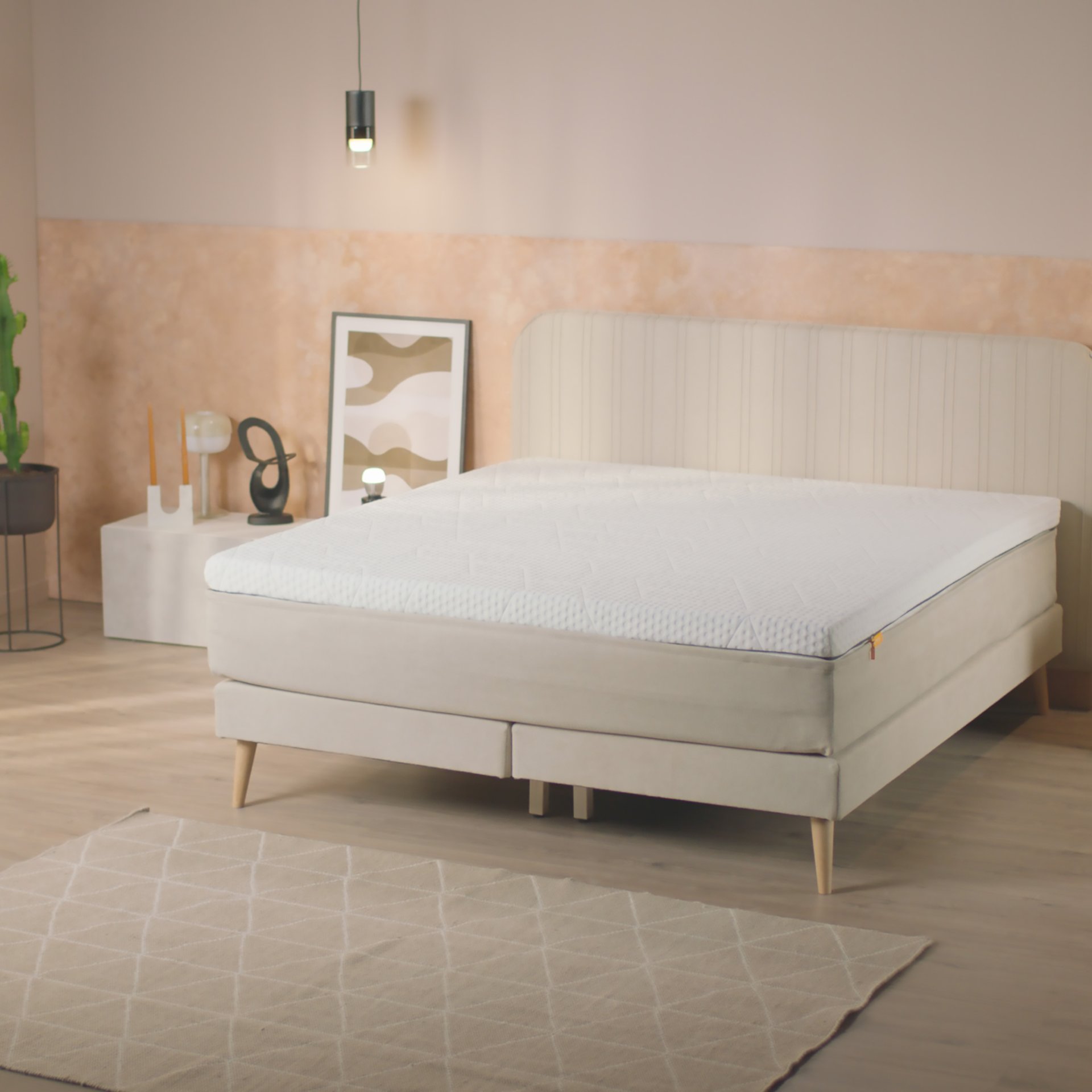 Camera moderna con letto chiaro, topper, tavolini decorati e luci sospese.