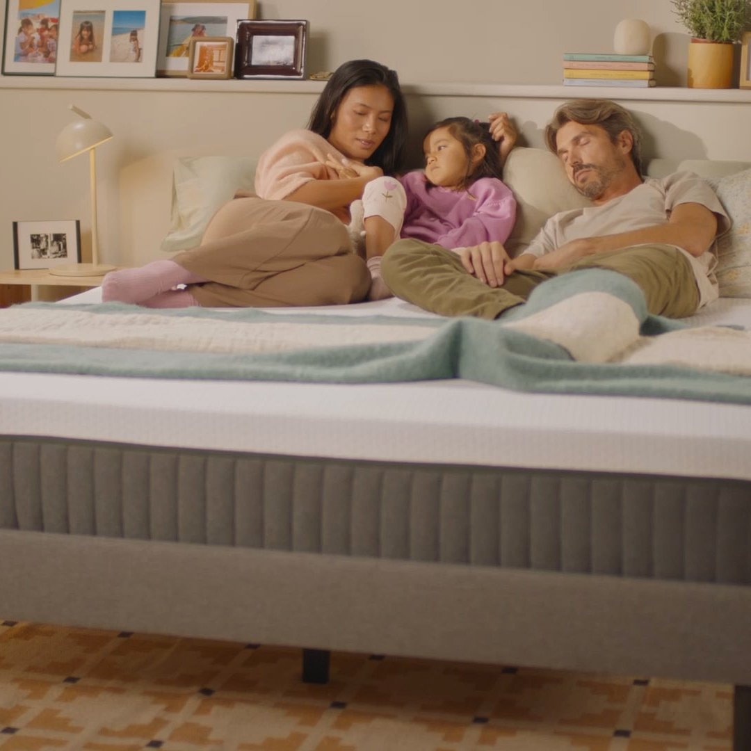 Person sitting up on a bed with a white mattress in the morning.