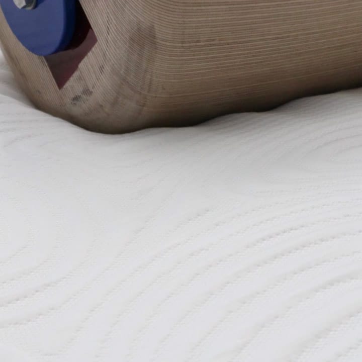 A heavy laboratory roller rolling over a white quilted mattress surface during durability testing.