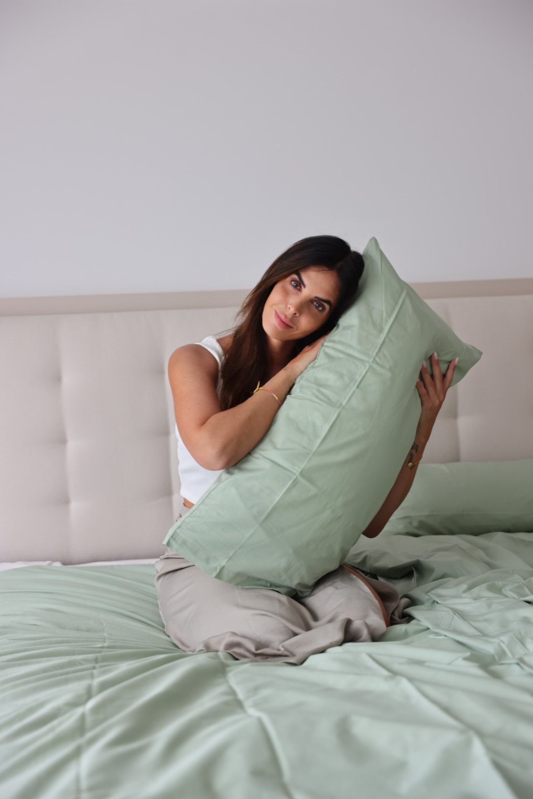 Frau kuschelt mit grünem Kissen auf Bett mit passender Bettwäsche in sanften Farbtönen.