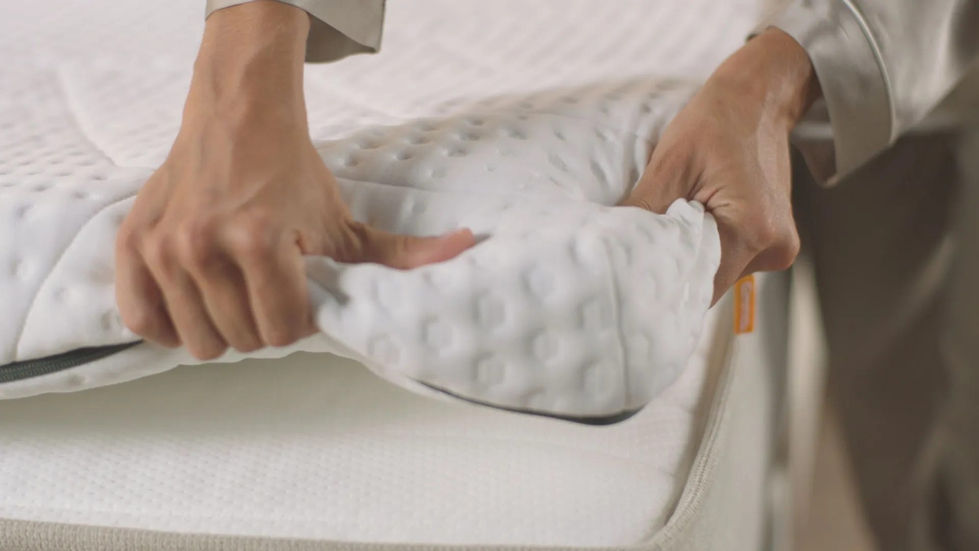 Deux mains ajustant un surmatelas blanc texturé sur un matelas.