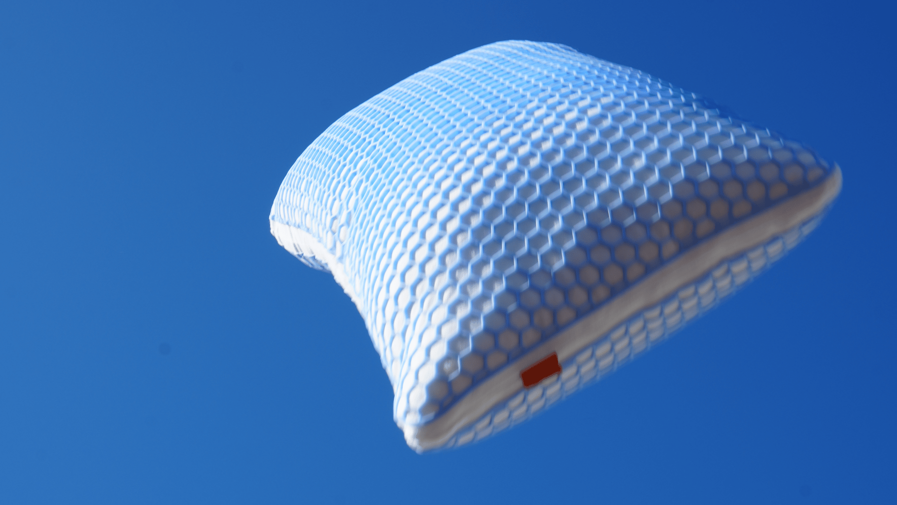 Ergonomisches Elite Kissen mit Wabenstruktur schwebt vor blauem Himmel.