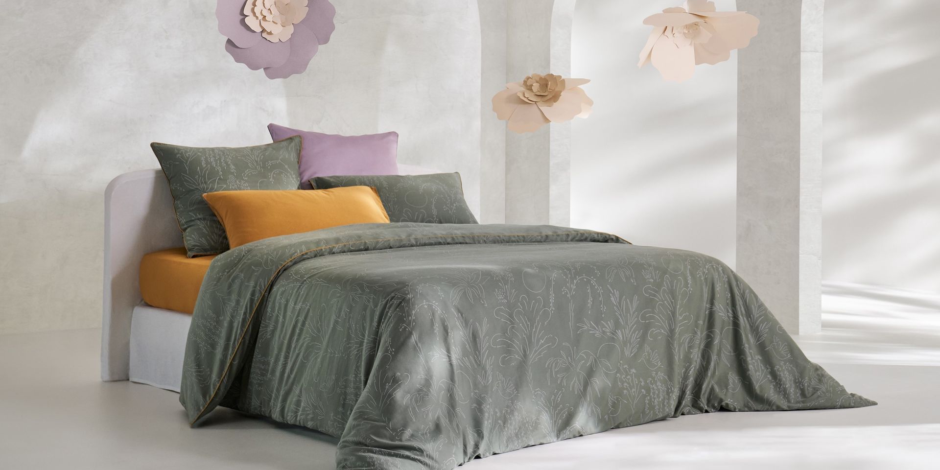 Chambre décorée avec des fleurs, lit gris clair avec une housse de couette florale et des oreillers colorés.