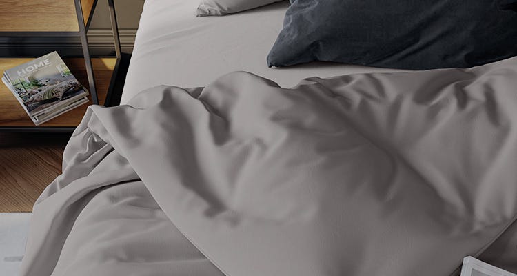 Slaapkamerhoek met een bed met grijze lakens en donkergrijze kussen; houten nachtkastje met tijdschriften, bovenste met titel "HOME".