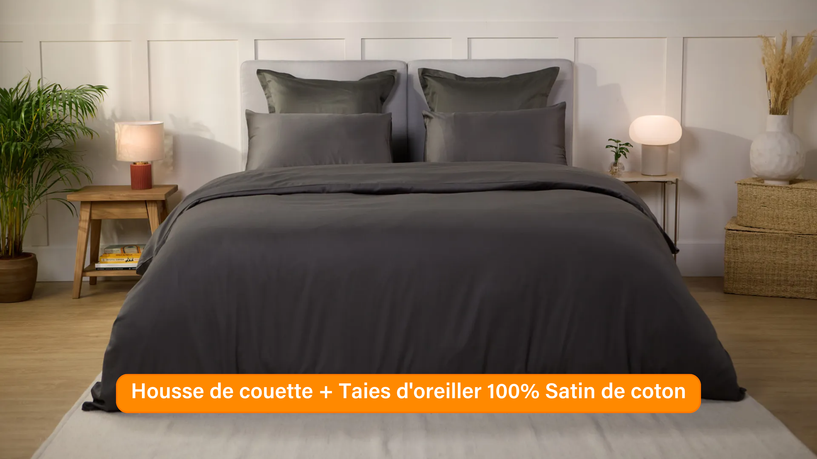 Chambre élégante avec lit soigneusement préparé, habillé d’une parure de lit 100 % satin de coton de couleur Gris Foncé. Plusieurs oreillers sont disposés contre un mur à panneaux. De chaque côté du lit, des tables de chevet avec lampe et objets décoratifs. Un banc rose est placé au pied du lit, assorti à un tabouret près de la table de chevet. Le sol en bois clair et les murs neutres créent une ambiance douce et raffinée.