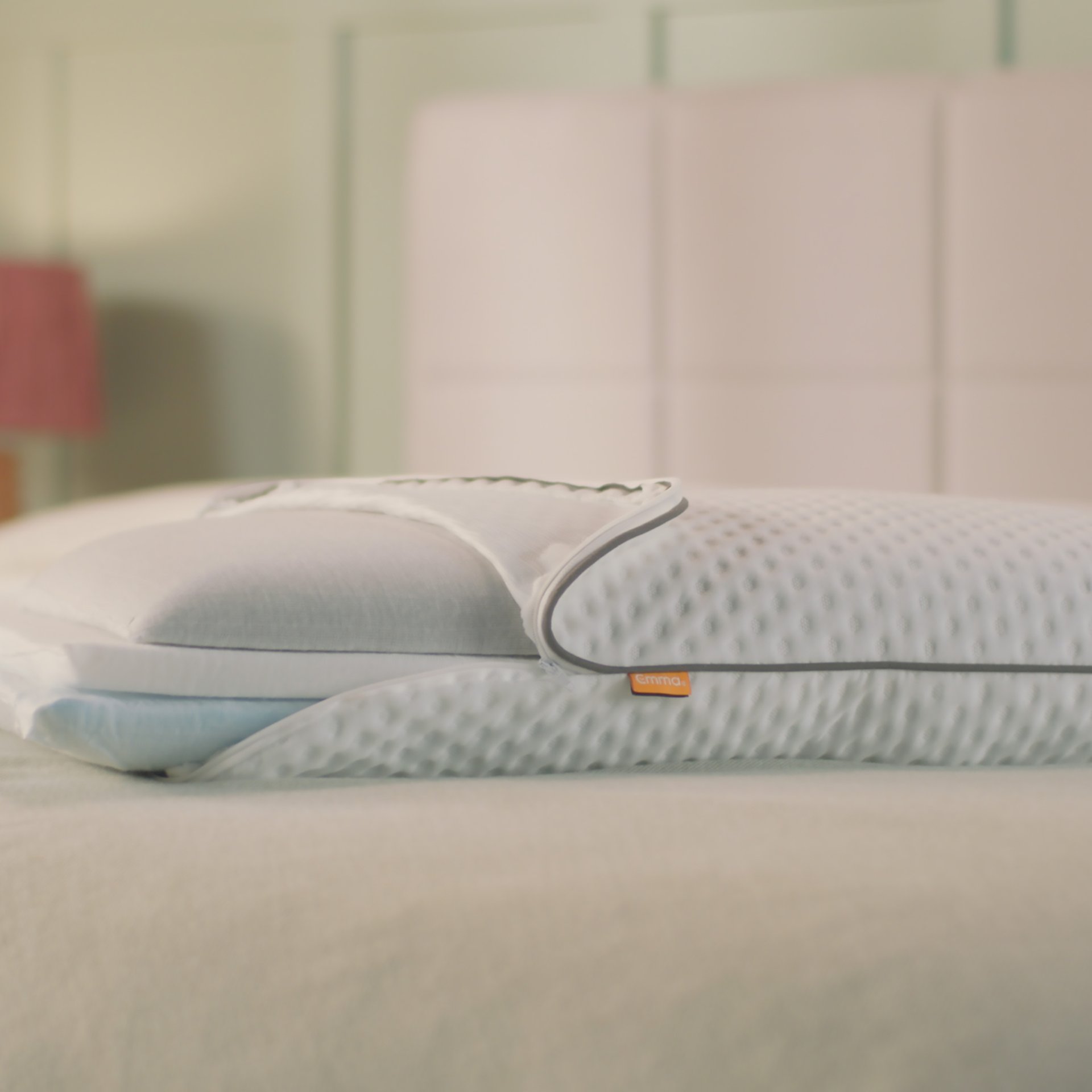 Oreiller Original Premium posé sur un lit fait, avec housse blanche texturée et étiquette orange.