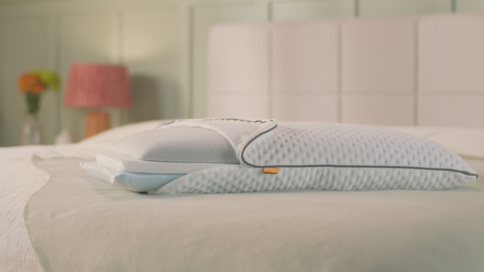 Oreiller Original Premium posé sur un lit fait, avec housse blanche texturée et étiquette orange.