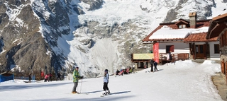 Personen auf Ski und Snowboard vor Berghütte im Aostatal.