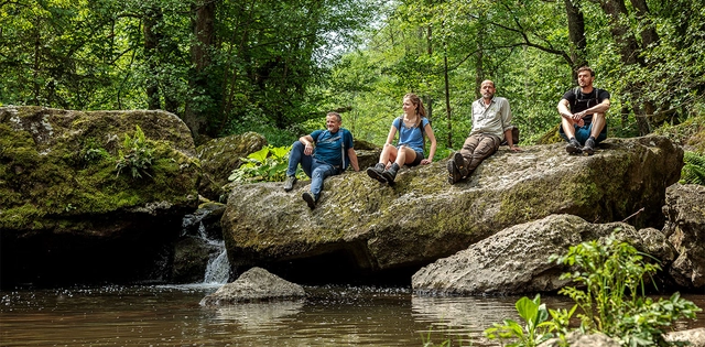 Menschen sitzend auf einem Felsen in einer Bachlandschaft im Grünen