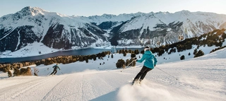 Skifahrer auf der Piste in der Zwei Länder Skiarena bei Abfahrt mit Ausblick auf den Reschensee.