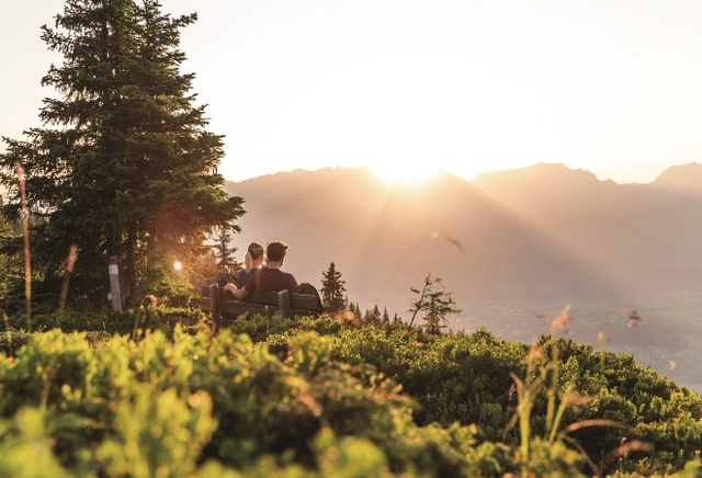 Zwei Personen genießen den Sonnenaufgang auf einer Bank