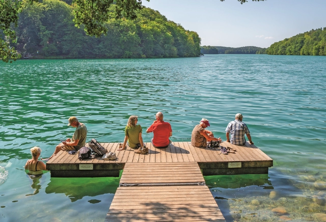 6.png Personen sitzen in der Sonne auf einem Steg am Wasser