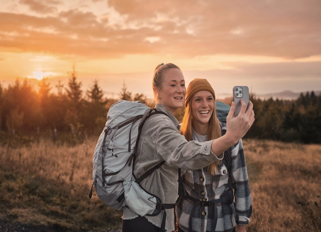 Zwei Wanderinnen machen ein Selfie zusammen vor einem Sonnenaufgang 