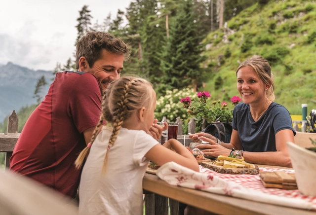 Eine kleine Familie sitzt am Essenstisch und verspeist eine Bretteljause