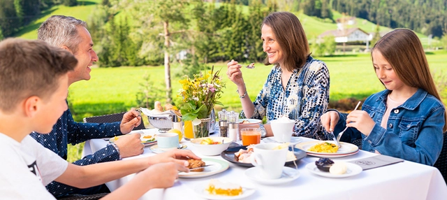 Familie beim Frühstück draußen im Grünen.