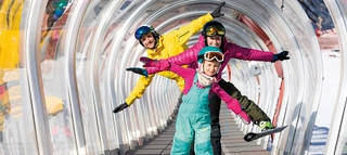 Drei Personen mit Ski bei Auffahrt mit Zauberteppich in der Region Seefeld.