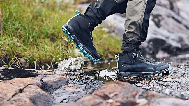 Aufmacher_Produkttest_Schuhe Leichter Schuh in schwarz blau während einer Wanderung über Steine durch ein Bachbett.