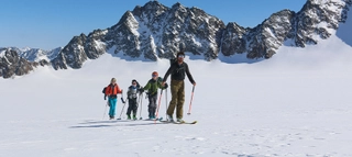 Vier Skitourengeher mit Bergen im Hintergrund.