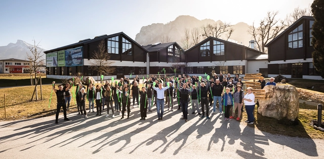 Gruppe von Personen mit Skistöcken in den Händen vor Gebäude und Bergen.