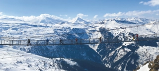 Brücke vor verschneitem Bergpanorama.