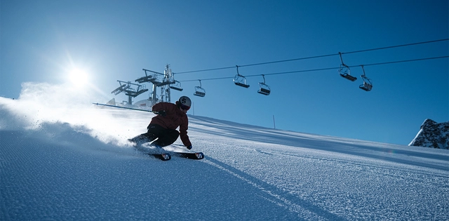 Skifahrer auf Piste mit Skilift im Hintergrund.