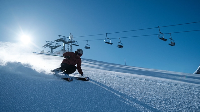 Skifahrer auf Piste mit Skilift im Hintergrund.