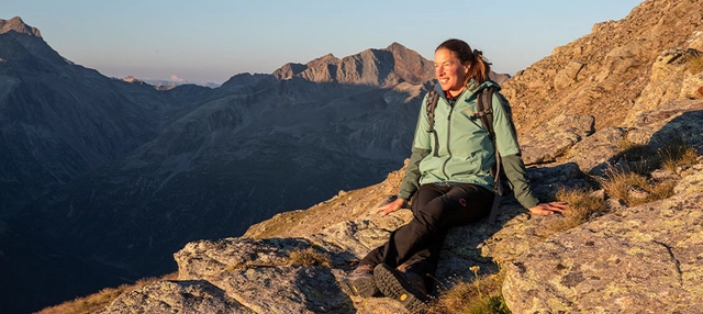 Wanderin sitzend auf Felsen in goldenem Licht während der Abendstimmung mit Blick in die Ferne.