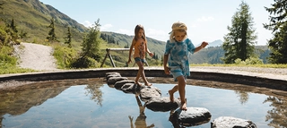 Teich im Lauserland Kinder springen über Steine Wasser Alpbach Wiedersbergerhorn