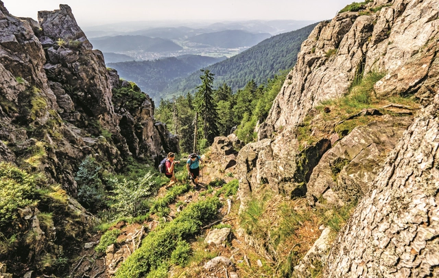 Zwei Wanderer laufen zwischen großen Felsformationen einen Berg hinauf