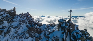 Bergkulisse mit Gipfelkreuz über den Wolken.