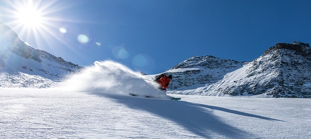 Skifahrer vor Bergkulisse bei Sonnenschein und tiefblauem Himmel.