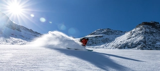 Skifahrer vor Bergkulisse bei Sonnenschein und tiefblauem Himmel.