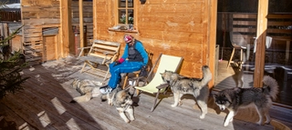 Person im Liegestuhl mit Huskys auf Holz-Terrasse.