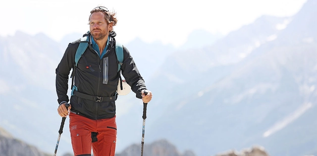 Männlicher Wanderer unterwegs in den Bergen mit Rucksack und Stöcken. Bekleidet mit Softshell Jacke.