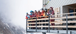 Gruppe Personen steht am Geländer der Mönchshütte in Winterkleidung.