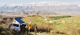 Zwei Personen mit Ski in der Hand neben Auto vor Natur- und Bergkulisse in Albanien.