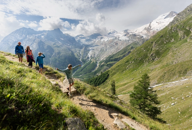 2.png Eine Familie auf einem sonnigen Wanderweg mit Bergpanorama im Hintergrund