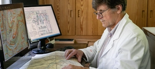 Kartograf Rolf Böhm vor zwei Bildschirmen mit Landkarten.