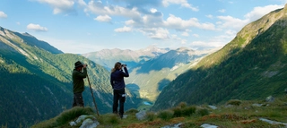Zwei Personen vor Bergkulisse in Kärnten, die mit Ferngläsern in die Ferne schauen.
