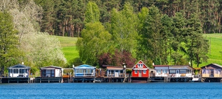 Bunte Häuser am Ufer des Sees mit Wald im Hintergrund.