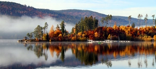 Inspirationen_Top10Herbstwege_Bild5_C-Shutterstock-GerhardAlbicker Gewässer und herbstliche Bäume vor Bergen.