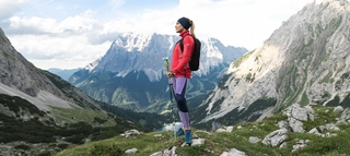 Weibliche Wanderin vor massiver Bergkulisse in Fleecejacke mit Wanderausrüstung.