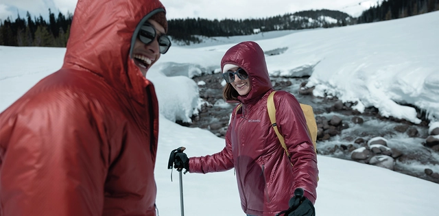 Zwei Personen neben einem Gewässer in einer verschneiten Winterlandschaft.