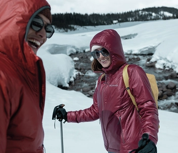 Zwei Personen neben einem Gewässer in einer verschneiten Winterlandschaft.